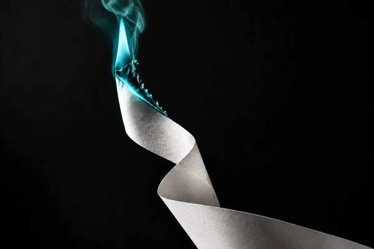 A paper receipt curling as its edge burns with a teal flame